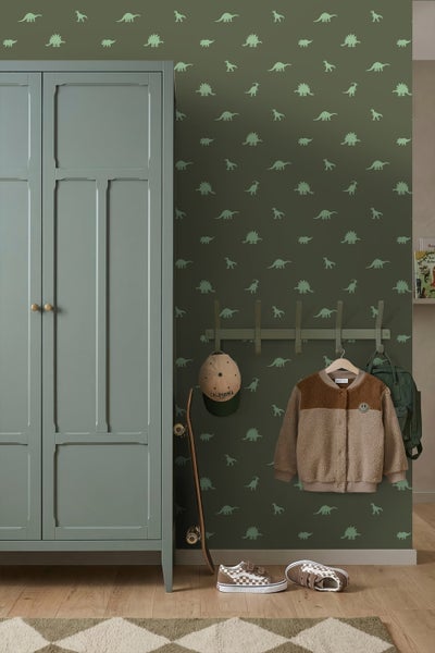 Vlies-Tapete mit Dinosaurier-Muster in einem organisierten Kinderzimmer neben einem Kleiderschrank aus Holz und einer Garderobe.