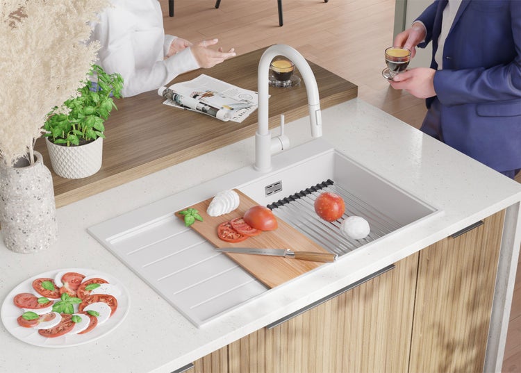 Küchenszene mit Spüle, Armatur, Schneidebrett, Tomaten, Mozzarella und Kräutern auf einer Küchentheke.