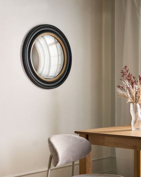Runder Wandspiegel mit breitem schwarzen Rahmen und goldenem Innenring in einem modern eingerichteten Raum.