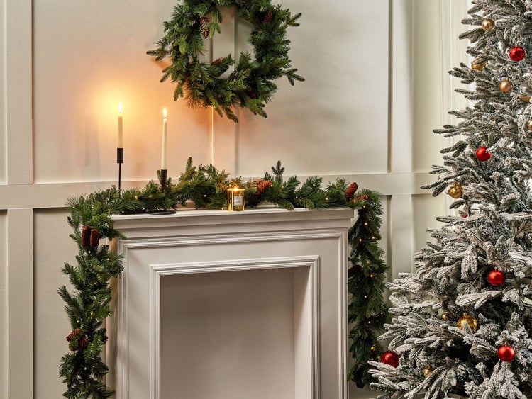 Weihnachtliche Dekoration mit beleuchtetem Kranz, Girlande mit Zapfen, Kerzen und geschmücktem Weihnachtsbaum.