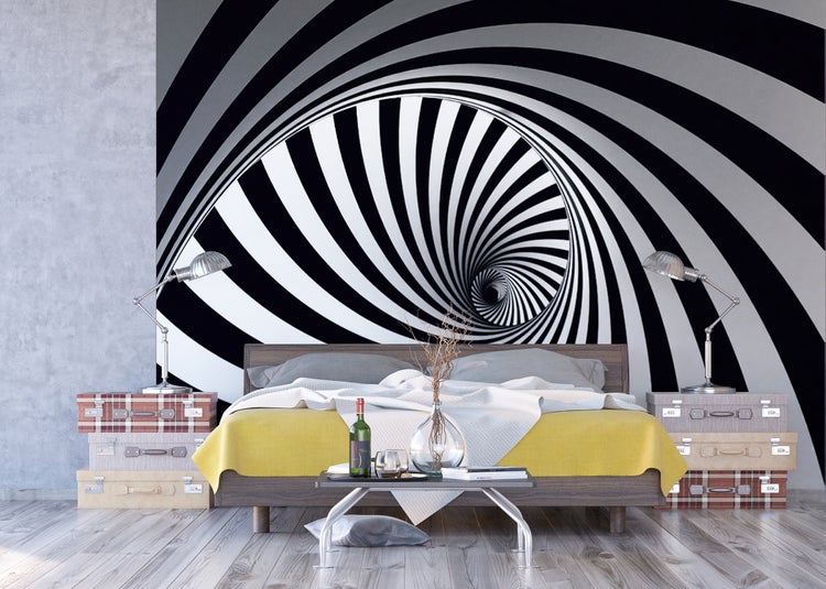 Schlafzimmer mit Bett, Nachttischen aus Koffern und einer schwarz-weissen Wandtapete mit Spiralmuster