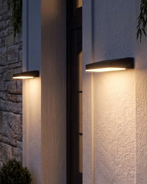 Moderne schwarze LED-Außenwandleuchten strahlen warmes Licht nach unten auf eine strukturierte Hauswand im Eingangsbereich.