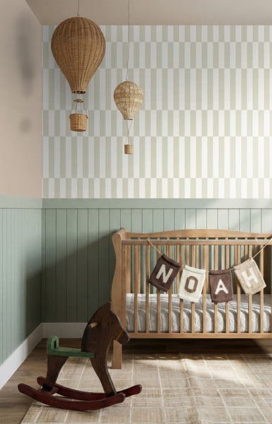 Helles Kinderzimmer mit gemusterter Vliestapete, grüner Wandtäfelung aus Holz, einem Gitterbett aus Holz und einem Schaukelpferd.