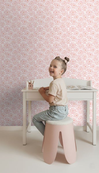 Kinderzimmer mit floraler Tapete mit Gänseblümchen-Muster. Ein Kind sitzt an einem weißen Schreibtisch vor der Wand.