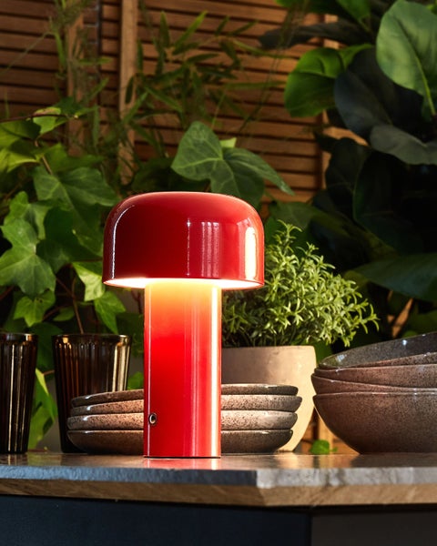 Rote Tischleuchte auf einem Tisch mit Schalen und Pflanzen im Hintergrund