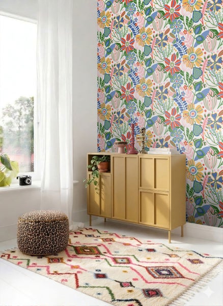 Helles Zimmer mit bunt blühender Vliestapete, einem gelben Sideboard, geometrisch gemustertem Teppich und einem Pouf in Leoparden-Optik.