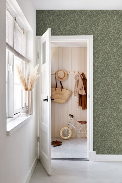 Vliestapete mit floralem Muster in einem hellen Flur mit weißer Tür, Holzpaneelen, Garderobe und einem Kinder-Laufrad.