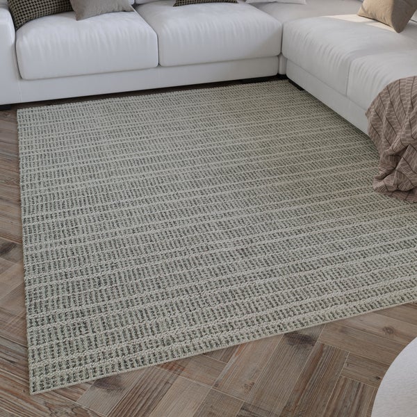 Rechteckiger Webteppich mit Strukturmuster vor einem Sofa auf Holzparkett in einem hellen Wohnzimmer.
