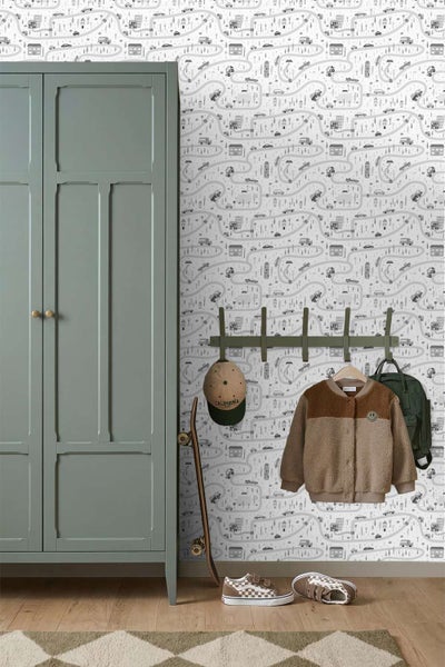 Kinderzimmer mit Tapete mit Straßenmuster und Häusern. Ein Kleiderschrank steht neben einem Wandhaken mit Kleidung, einer Mütze und einem Rucksack.