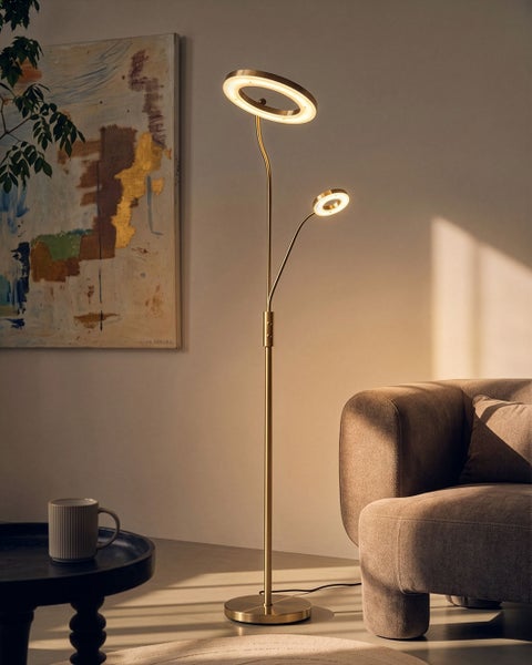 Moderne Stehlampe aus Metall mit zwei runden LED Lichtelementen im Wohnzimmer neben einem Sessel und einem Beistelltisch mit Tasse.