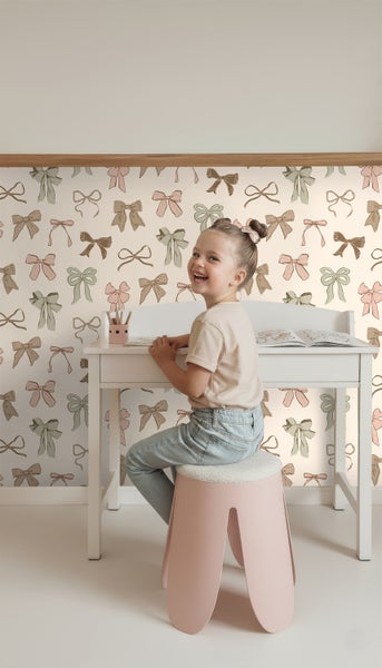 Mädchen sitzt an einem Schreibtisch vor einer Wand mit Schleifen Tapete
