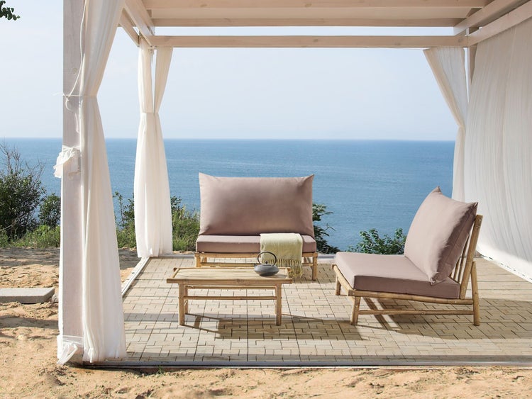 Sitzgruppe mit Bambusgestell unter einem Pavillon mit weißen Vorhängen, Blick auf das Meer.