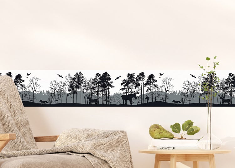 Tapetenbordüre mit Wald-Silhouette-Motiv in einem hellen Wohnzimmer mit Sofa und Holztischen.
