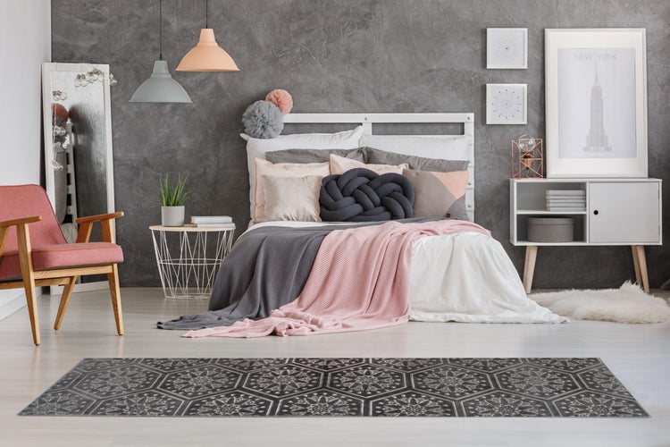 Modernes Schlafzimmer mit grauer Strukturwand, weißem Bett, rosa Sessel und einem gemusterten Teppichläufer im Vordergrund.
