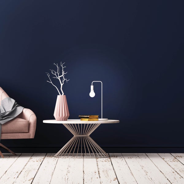 Dekoratives Wohnzimmer mit Sessel, Beistelltisch, Lampe und Dekorationen vor einer dunklen Wand.
