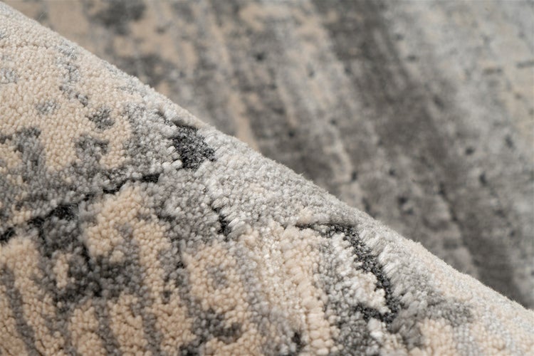 Nahaufnahme eines grauen Teppichs mit abstraktem Muster, hellen Fransen und gewebter Rückseite.