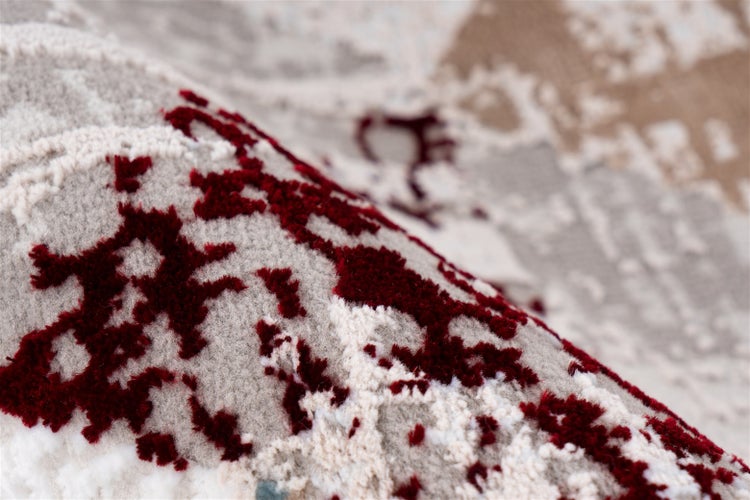 Detailaufnahme eines strukturierten Teppichs mit abstraktem Muster in Rot, Grau und Beige.