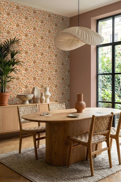 Helles Esszimmer mit floraler Vlies-Tapete, ovalem Holztisch, geflochtenen Stühlen, großer Pendelleuchte und Sideboard aus Holz.