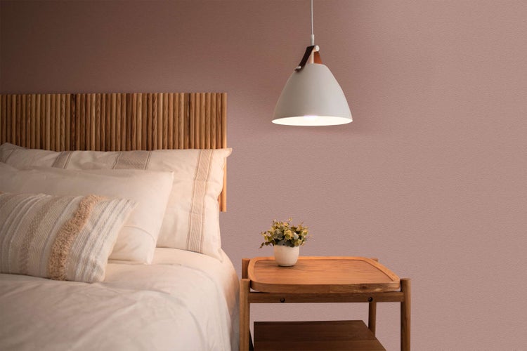 Schlafzimmer mit strukturierter altrosa Wand, Holzkopfteil, Nachttisch aus Holz und einer modernen Pendelleuchte in Weiß.