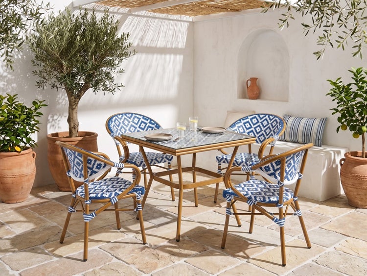 Gartenmöbel-Set mit quadratischem Glastisch und vier Stühlen mit blau-weißem Geflecht in geometrischem Muster auf einer mediterranen Terrasse.