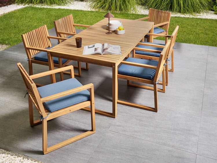 Gartenmöbel-Set aus Holz bestehend aus einem rechteckigen Esstisch und sechs Stühlen mit Armlehnen und Sitzkissen auf einer Terrasse.