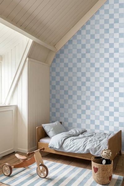 Helles Kinderzimmer mit blau-weiß karierter Tapete, einem Holzbett mit gestreifter Bettwäsche und einem Holzspielzeug auf einem Teppich.