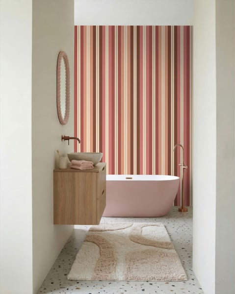 Modernes Badezimmer mit gestreifter Tapete in Rosa- und Brauntönen, freistehender Badewanne, Holzwaschtisch und Terrazzoboden.
