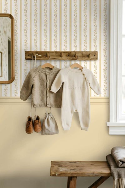 Wohnraum mit gestreifter Blumentapete an der Wand, kombiniert mit einer hölzernen Garderobenleiste und hängender Kinderkleidung im Landhausstil.