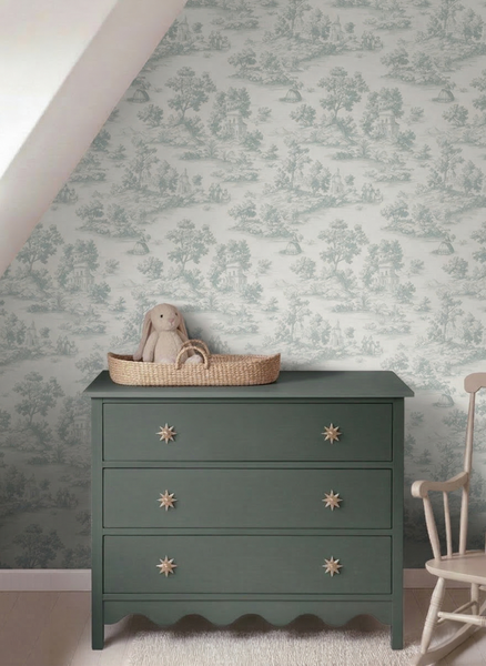 Vliestapete mit Toile-de-Jouy-Muster in einem hellen Kinderzimmer hinter einer dunkelgrünen Kommode mit Sternknöpfen.