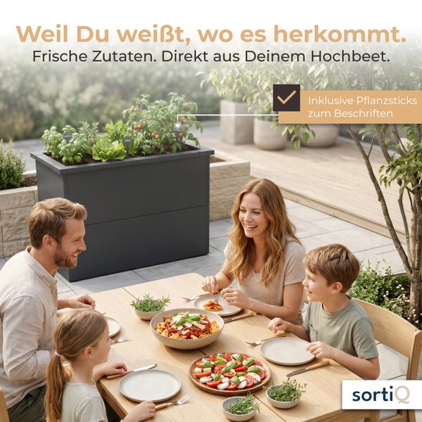 Familie beim Essen auf der Terrasse neben einem anthrazitfarbenen Hochbeet aus Metall mit Kräutern und Gemüse. Inklusive Pflanzsticks. sortiQ Logo.