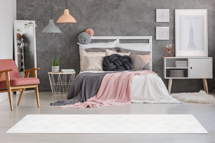 Modern eingerichtetes Schlafzimmer mit weißem Bett, rosa Sessel, Drahtbeistelltisch, Pendelleuchten, strukturierter grauer Wand und hellem Teppich.