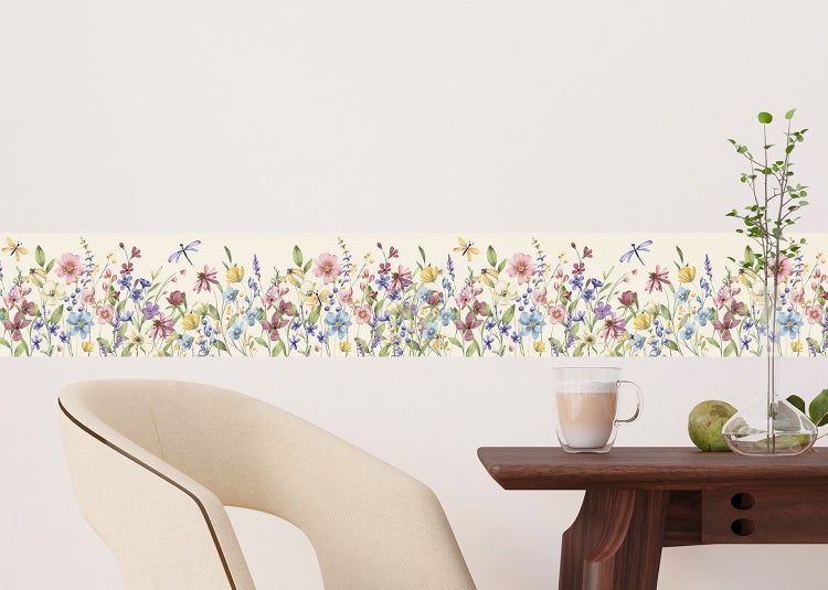 Selbstklebende Tapetenborte mit Wildblumen- und Libellenmuster in einem hellen Raum mit Holztisch und Sessel.