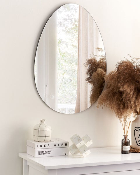 Ovaler Spiegel mit schlankem Rahmen an der Wand über einer Kommode mit Dekorationsartikeln