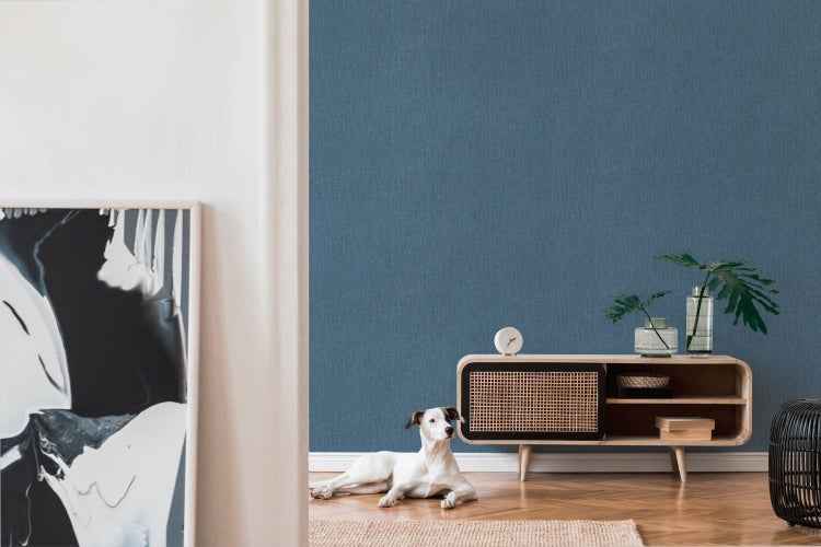 Wohnzimmer mit blauer Textiltapete, Kommode und liegendem Hund auf dem Boden