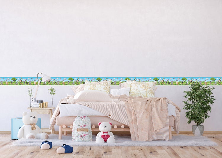 Helles Kinderzimmer mit Wandbordüre mit Tiermotiven, einem Bett mit Bettwäsche, Teddybären auf einem Teppich und einer Zimmerpflanze.