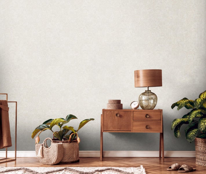 Heller Raum mit Kommode, Lampe, Pflanzen und Dekorationsartikeln vor einer strukturierten Tapete.