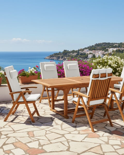 Gartenmöbel Set aus Holz mit einem rechteckigen Tisch und vier Klappstühlen mit weißen Auflagen auf einer hellen Steinterrasse mit Meerblick.