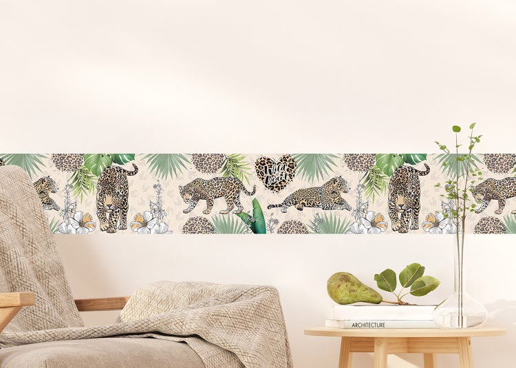 Selbstklebende Tapetenbordüre mit Leoparden-Motiv, Palmblättern und exotischen Blumen in einem hellen Wohnraum angebracht.