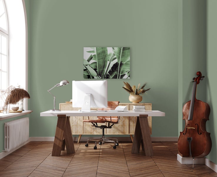 Modernes Heimbüro mit grün gestrichenen Wänden, Schreibtisch aus Holz, Computer, Schreibtischlampe, Lederstuhl, Sideboard und einem Kontrabass.
