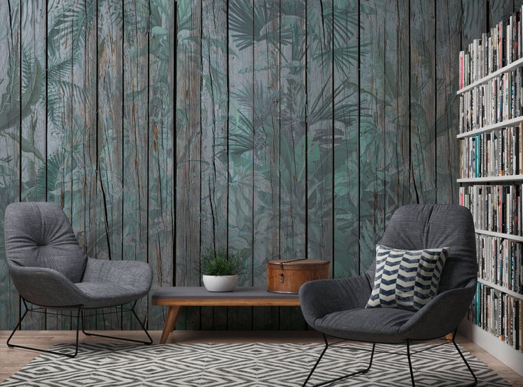 Fototapete mit Holzplanken- und Palmenblatt-Motiv in einem modern eingerichteten Wohnzimmer mit zwei grauen Sesseln und einem Bücherregal.