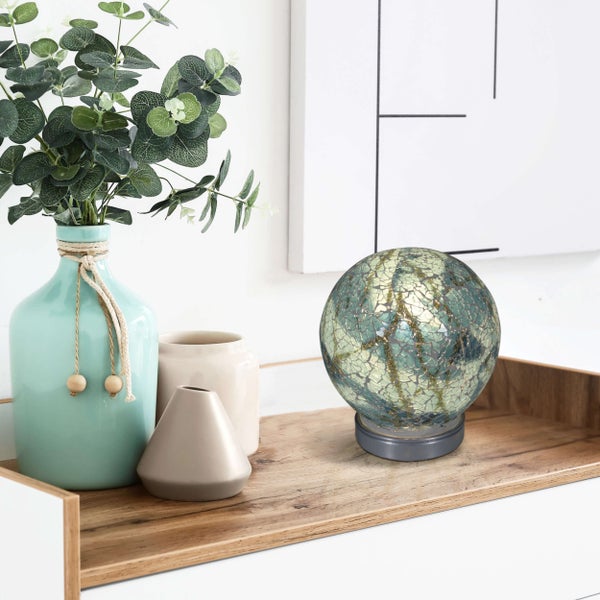 Dekorative Szene mit Vase, Pflanzen, Kerzen und einer dekorativen Glaskugel auf einem Holztablett.