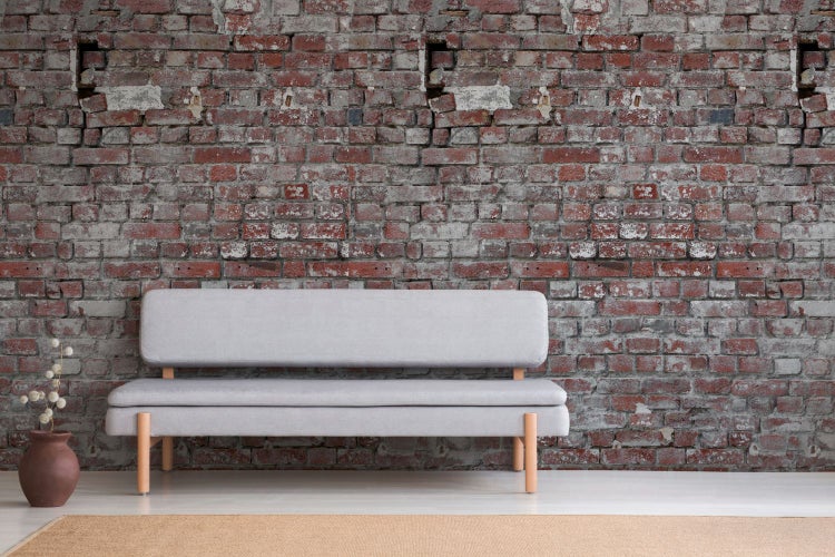 Graues Sofa vor einer roten Backsteinmauer als Raumgestaltungselement