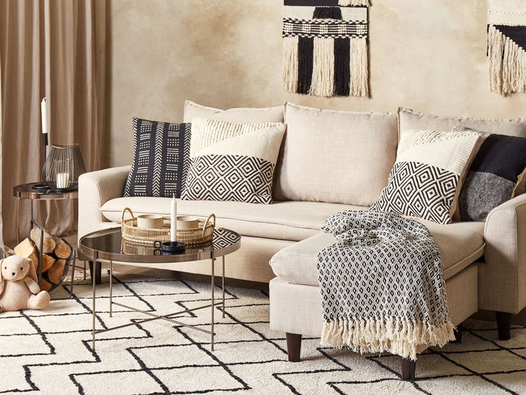 Modernes Wohnzimmer im Boho-Stil mit hellem Sofa, schwarz-weißen Kissen, gemustertem Teppich, rundem Couchtisch und dekorativem Wandbehang.