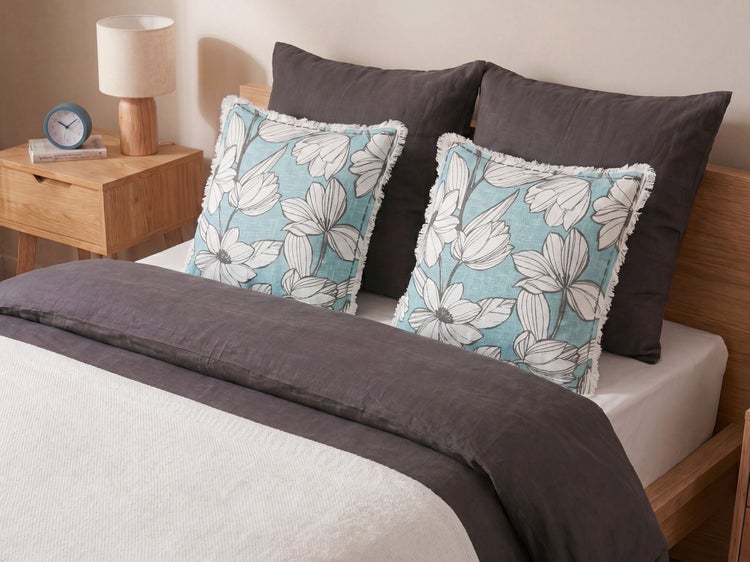 Modernes Schlafzimmer mit Holzbett, dunkelgrauer Bettwäsche und dekorativen Zierkissen mit Blumenmuster. Ein Nachttisch aus Holz steht daneben.