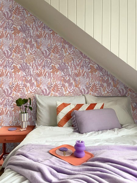 Ein Schlafzimmer unter einer Dachschräge mit einem Bett, Nachttisch, Kissen und einer gemusterten Tapete.