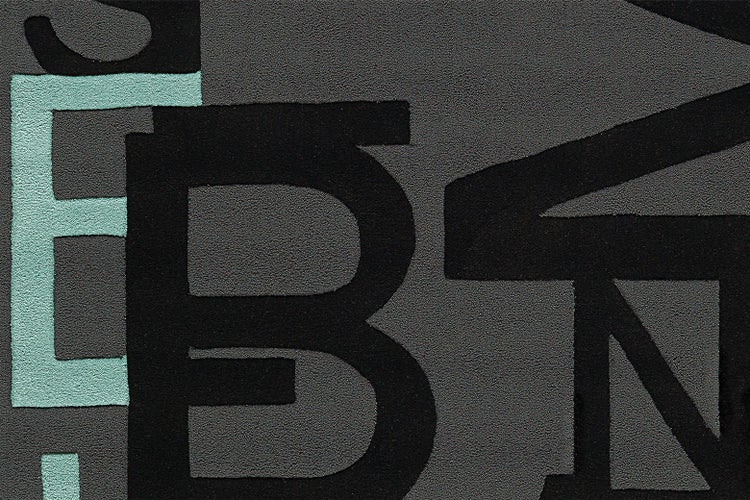 Detailaufnahme eines strukturierten Teppichs mit einem Buchstabenmuster in Schwarz und Türkis.