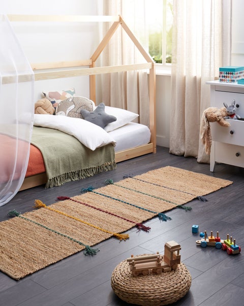 Läufer aus Naturfaser mit bunten Streifen und Quasten in einem hellen Kinderzimmer mit Hausbett und Holzspielzeug.