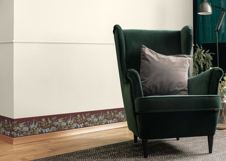 Tapetenbordüre mit Blumenmuster an einer hellen Wand im Wohnzimmer mit grünem Samtsessel und Holzfußboden.