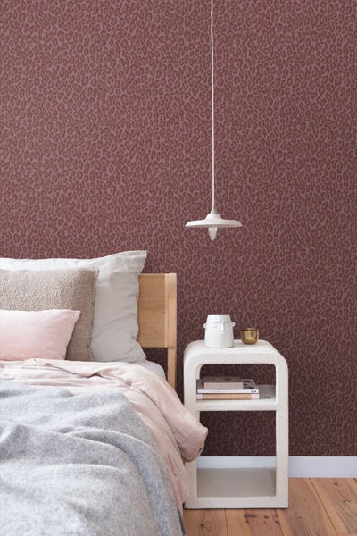 Vliestapete mit Leopardenmuster in einem hellen Schlafzimmer mit Bett, Nachttisch und Pendelleuchte.