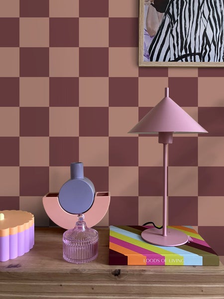 Dekorative Gegenstände auf einem Holzregal vor einem Schachbrettmuster an der Wand.